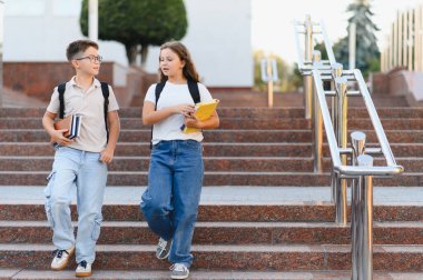 Sırt çantalı ve kitaplı öğrenciler açık hava üniversitesinin merdivenlerinden iniyorlar, derslerden sonra aktif olarak sohbet ediyorlar.