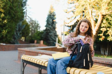 Liseli kız kameraya bakıyor, sırt çantasından malzemeleri alıyor. Sınıf için hazırlanılıyor ya da yolculuğa başlanıyor