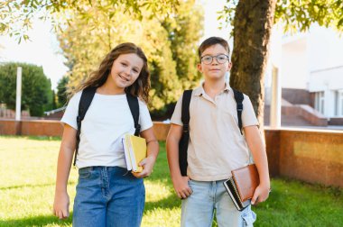 Okul çocukları kampüste birlikte duruyorlar, sırt çantaları ve kitaplar taşıyorlar, eğitime ve eğitime hazırlar.