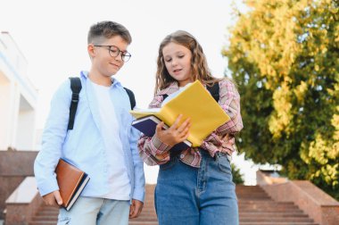 İki okul çocuğu, bir oğlan ve bir kız, kampüs merdivenlerinde duruyorlar, ellerinde kitap tutarken ve okurken dersleri tartışıyorlar.