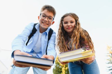 Gülümseyen okul çocukları, bir kız ve bir erkek izleyiciye kitap uzatıyor, öğrenmeyi, bilgiyi ve okulu simgeliyor.