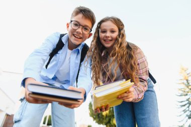 Mutlu okul çocukları kitap sunuyor ve gülümsüyor, eğitim, öğrenme ve okul kavramlarına geri dönüyor.