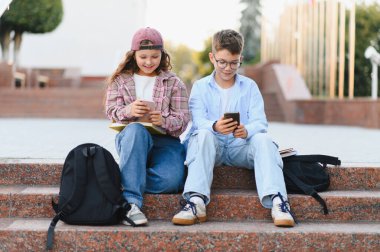 Okul arkadaşları okul dışında oturuyor, cep telefonları kullanıyorlar, cep telefonu teknolojisine bağlanıyorlar ve internetten öğreniyorlar.