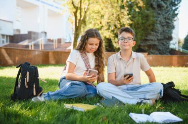 Okul çocukları okul kampüsünde vakit geçiriyorlar. Mola sırasında akıllı telefonları eğlence ya da iletişim için kullanıyorlar.