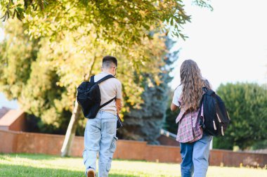 Okul kampüsüne giden sırt çantalı öğrenciler, eğitimi, arkadaşlığı ve okul konseptini temsil ediyorlar.