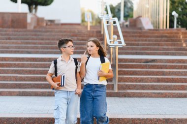 Okul merdivenlerinden aşağı inen iki genç öğrenci, sırt çantaları ve kitaplarla, dersten önce arkadaşça sohbet ediyorlardı.