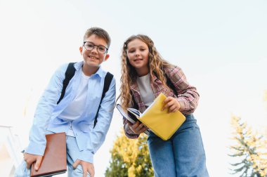 Sırt çantaları ve kitaplarıyla dışarıda dikilen mutlu okul çocukları öğrenmeye ve okula dönmeye hazırlar.