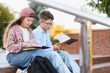 İki okul çocuğu dışarıda basamaklarda oturuyor, kitaplar okuyor ve dersleri tartışıyorlar, öğrenme aşkı geliştiriyorlar.