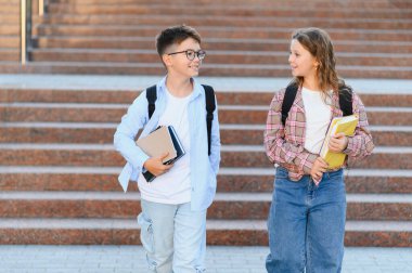 Dışarıda gezen, kitap tutan ve sırt çantası takan mutlu öğrenciler. Okula dönüş için arkadaşlık ve eğitim kavramı