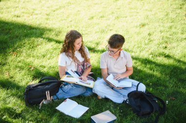 Çocuklar kitap okuyor ve güneşli bir günde dışarıda ödevlerini tartışıyorlar. Eğitim, bilgi ve sağlıklı yaşam tarzı kavramı