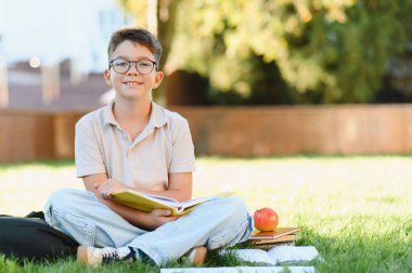 Yeşil çimlerin üzerinde oturmuş kitap okuyan mutlu öğrenci. Çocukluk eğitimi ve öğrenci yaşam tarzı konsepti