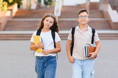 Öğrenmeye ve eğitime hazır gülümseyen okul çocukları. Öğrenciler sırt çantaları ve ders kitaplarıyla okula gidiyorlar.