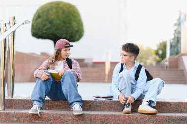 İki okul çocuğu okul merdivenlerinde oturmuş, kampüsteki bir eğitim molasında bir tartışmayı paylaşıyorlar.