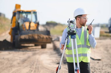 Güvenlik yeleği giyen ve kasketli bir adam tüm istasyonu tarıyor. İnşaat alanındaki telsizle iletişim kuruyor.