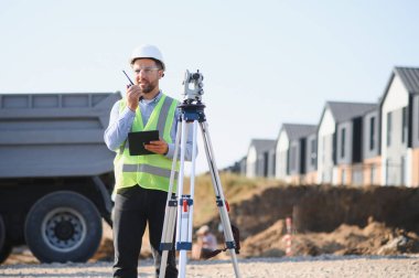 Elinde tablet ve telsiz olan erkek araştırmacı, bir inşaat alanında talimatlar veriyor.