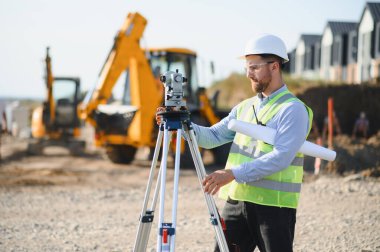 Yeni bir bina geliştirme, doğru ölçümler ve proje ilerlemesi sağlamak için araştırma ekipmanı kullanan profesyonel mühendis