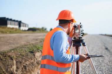 İnşaat mühendisliği şantiyesinde arazi ölçümü ve haritalama için toplam istasyon aleti kullanan bir arazi mühendisi.