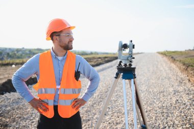 Erkek arazi ölçümü için bir teodolit kullanan ve yeni yol yapımına hazırlanan sert şapka ve güvenlik yeleği giyen arazi mühendisi.