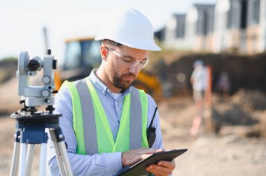 İnşaat mühendisi çelik yelek giyiyor. Civardaki dijital tablete bakıyor.