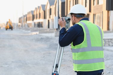 Araziyi incelemek ve yeni bir inşaat sahasını yerle bir etmek için teodolit kullanan bir araştırmacı.