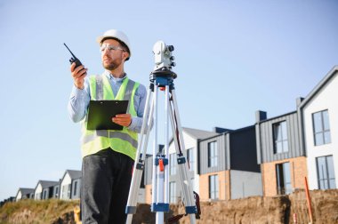 Güvenlik ekipmanı takan arazi ölçümü için telsiz ve teodolit kullanan bir arazi mühendisi.