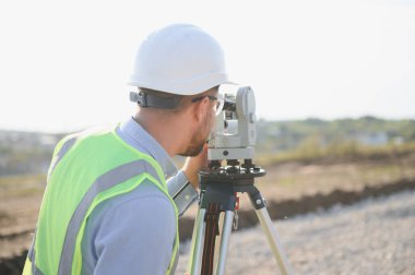 Bir inşaat sahasında teodolit ya da toplam istasyon ile çalışan profesyonel arazi araştırmacısı, doğru ölçümleri sağlamaktadır.