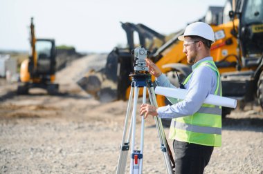 Mühendis arazi ölçümü ve yeni bir geliştirme projesi için araştırma ekipmanı kullanıyor, kesin inşaatı sağlama alıyor.