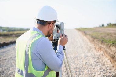 Arazi ölçümü ve inşaat mühendisliği projesi sahasında haritalama için teodolit kullanan bir araştırmacı