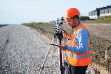 Bir inşaat sahasında çalışan profesyonel bir araştırmacı, telsizle iletişim kuran ve anket verilerini bir panodan kontrol eden.