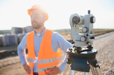 Jeodezi mühendisi güvenlik teçhizatı giyiyor ve arazi taraması ve yeni yol inşaatı için profesyonel toplam istasyonu kullanıyor.