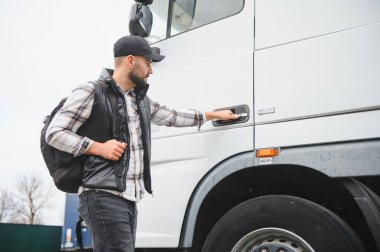 Sırt çantalı genç adam beyaz bir tırın kapısını açıyor, nakliye için hazır.