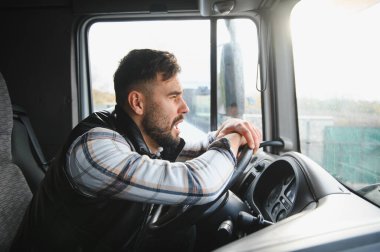 Kamaradaki kamyon şoförü trafiğe bağırıyor, gergin ve sinirli bir şekilde uzun bir yolculuk sırasında direksiyonu tutuyor.