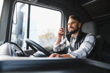 Profesyonel kamyon şoförü ağır bir araç kullanıyor ve telsizle konuşuyor. Lojistik ve nakliye işine olan bağlılığını gösteriyor.