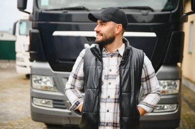 Gülümseyen bir adam, profesyonel bir kamyon şoförü, ağır bir yük kamyonunun önünde güven içinde poz veriyor. Ulaşım ve teslimat kavramı
