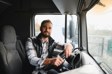 Sakallı ve fanila gömlekli bir adam kamyonet kullanıyor. Profesyonel kamyon şoförü malları uzun yoldan taşıyor.