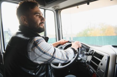 Önündeki yola odaklanmış ticari bir kamyonu kullanan bir adam. Uzun mesafeli ulaşım ve profesyonel sürüş mesleğini temsil ediyor.