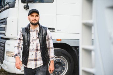 Profesyonel bir adam, kep ve yelek giyiyor, bir nakliye terminalinde büyük beyaz bir ticari kamyonun yanında duruyor.