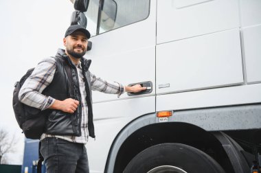Kamyon kabin kapısını açan sırt çantalı ve kareli gömlekli adam. Lojistik ve ulaşım sektöründe profesyonel sürücü.