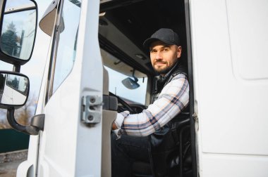 Kamyon şoförü kamyon kulübesinde oturuyor, kameraya bakıyor ve gülümsüyor. Ulaşım ve lojistik kavramı