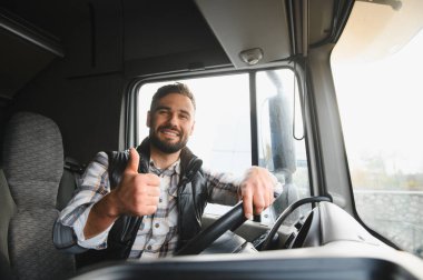 Aracında oturan mutlu erkek kamyon şoförü, gülümsüyor ve uzun bir yolculuğa hazır bir jest yapıyor.