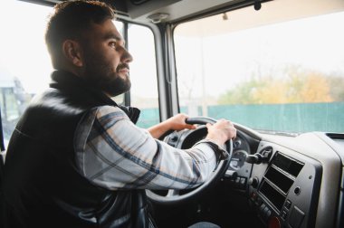 Adam ağır bir aracı kullanıyor, kargo taşıyor, lojistik sektöründe çalışıyor, odaklanmış görünüyor.