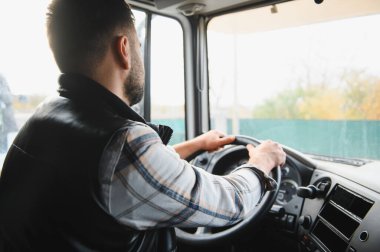 Adam içerideki kulübeden büyük bir kamyon sürüyor, ilerideki yola odaklanıyor. Profesyonel kargo taşımacılığı