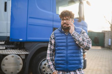 Genç bir kamyon şoförü büyük bir tırın yanında telefon görüşmesi yapıyor. Mal ve lojistik konsepti dağıtmak