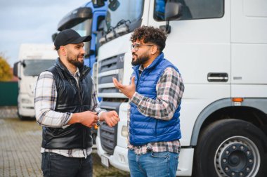 İki erkek kamyon şoförü dışarıda konuşuyor, büyük kamyonların önünde duruyorlar, modern ulaşım ve takım çalışmasını resmediyorlar.