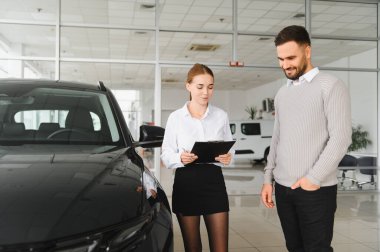 Arabayı erkek müşteriye gösteren satıcı, yeni araç özellikleri ve otomobil galerisindeki seçenekler hakkında bilgi veriyor