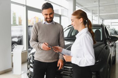 Müşteri gülümsüyor, modern bir araba galerisinde kadın bir satıcıyla kontrat imzalamaya hazır, yeni bir otomobil alıyor.