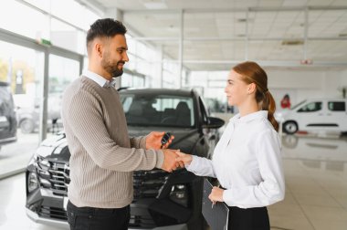 Yeni araba alımını tamamlayan, anahtarlarını alan ve bayiyle el sıkışan mutlu bir müşteri.
