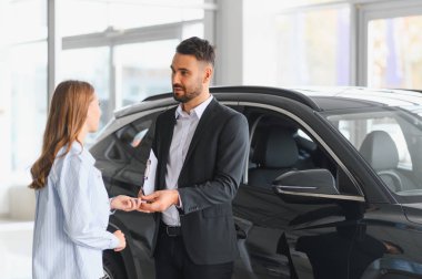 Profesyonel satıcı, başarılı bir satın alımdan sonra modern bir galeride mutlu bir kadına araba anahtarı veriyor.