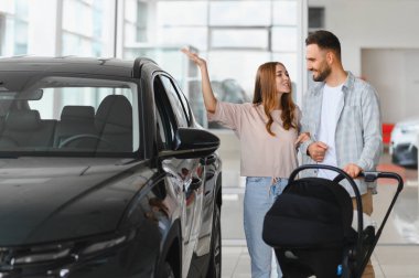 Bebek arabalı genç çift yeni bir cip seçiyor, araba galerisinde aile arabası arıyorlar.