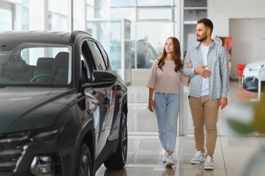 Genç bir çift, yeni bir araç satın alma seçeneklerini incelerken göz gezdirip gülümsüyor.